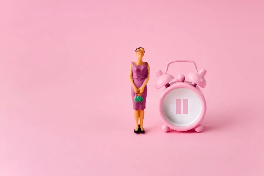 Miniature woman beside a pink alarm clock on a pink background